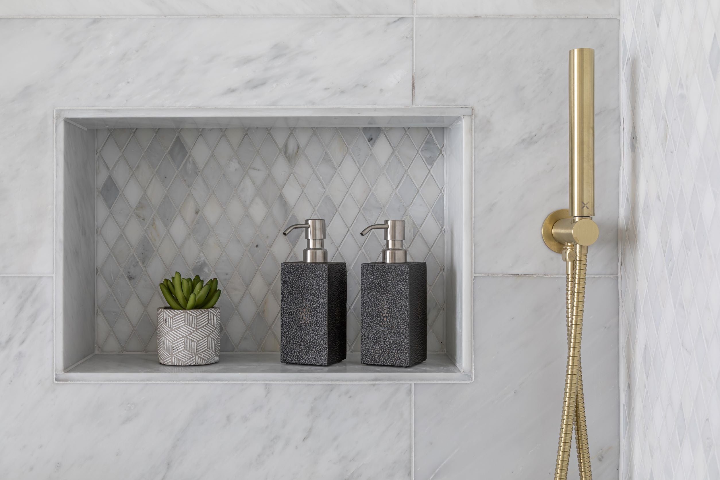 luxury bathroom accessories displayed on a tiled shelf by a gold shower head