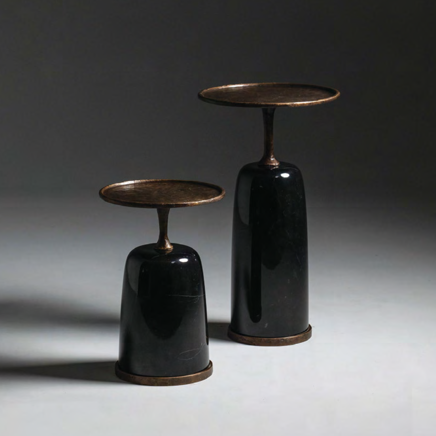 Two black side tables with bronze accents on a gray background